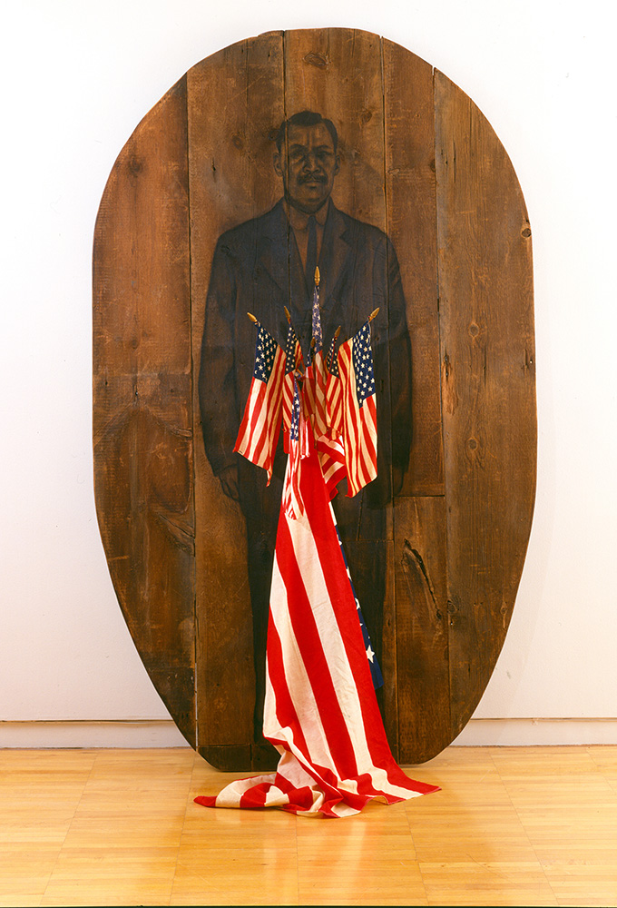 Photo of an large, oval-shaped wood slab adorned with a drawing of a man and several American flags.