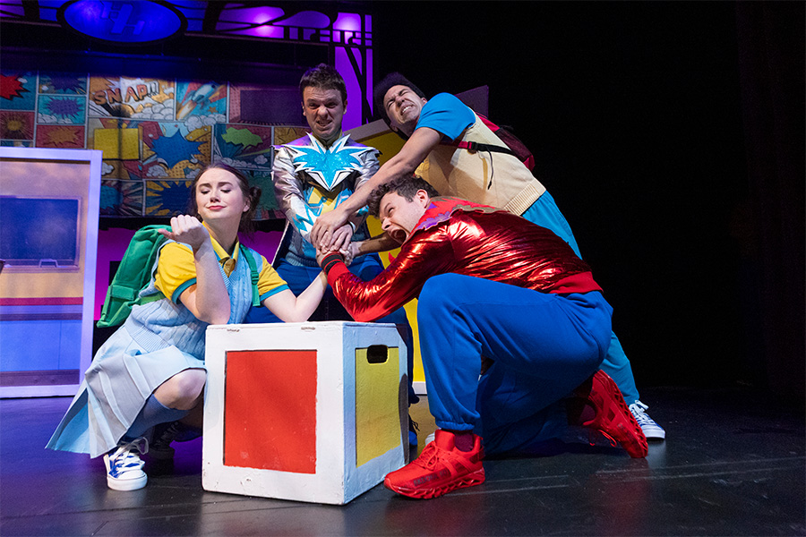 Photo of a group of four people dressed as superheroes performing on a stage.