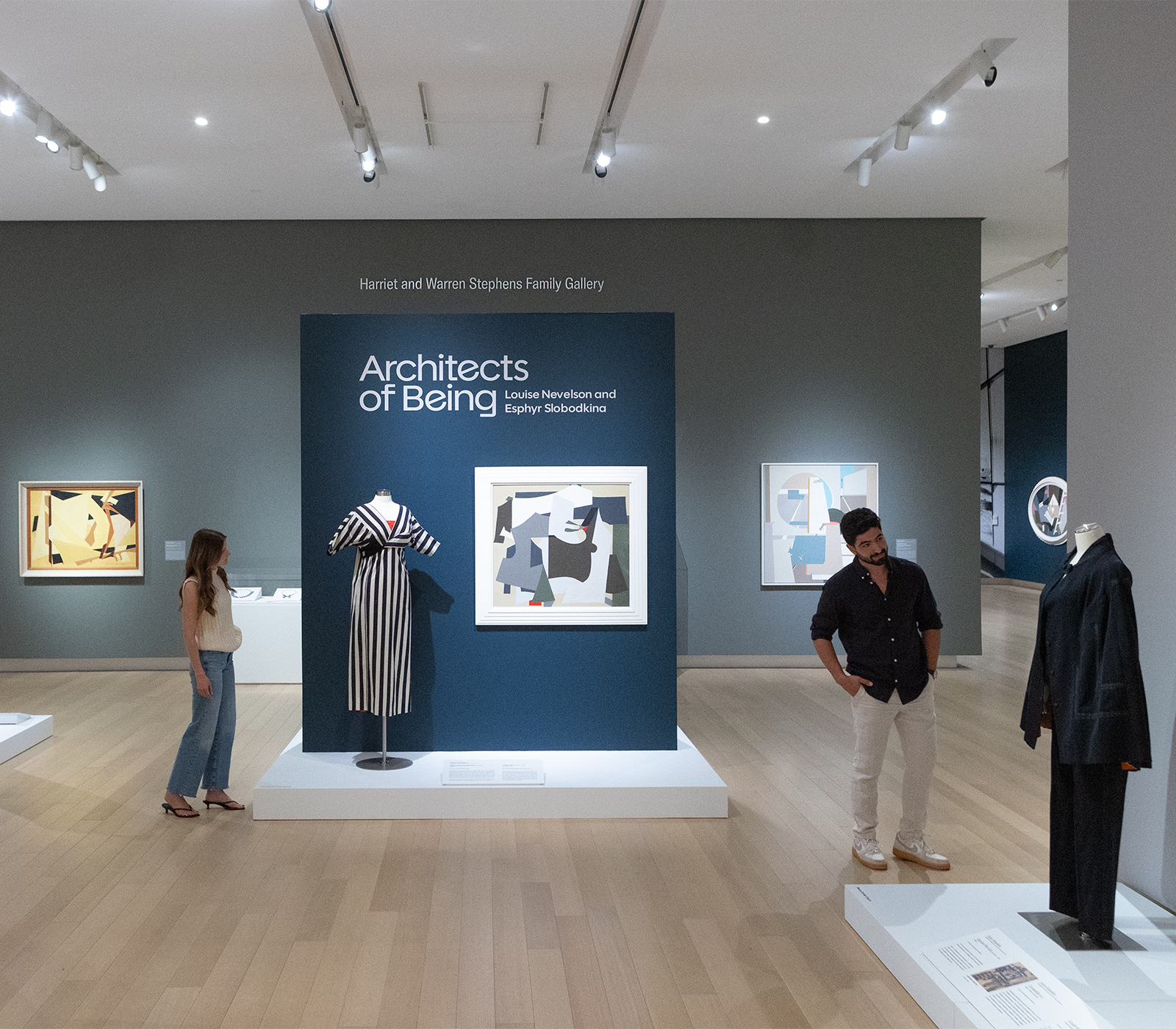 Photo of a man and a woman in an art gallery at AMFA looking at two different dresses on mannequins.