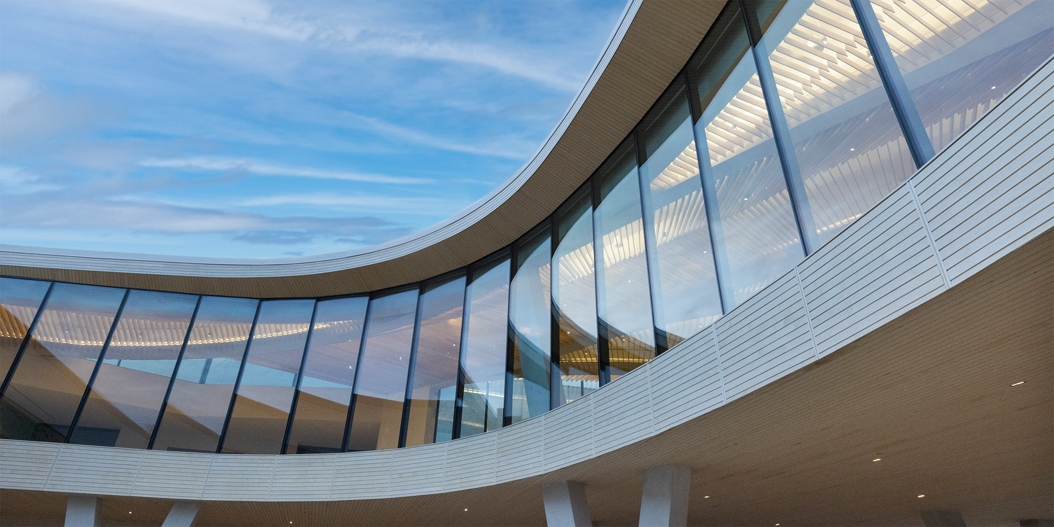 Architectural photo of the Cultural Living Room at AMFA viewed from outside. The room is curved and has dozens of floor to ceiling windows.