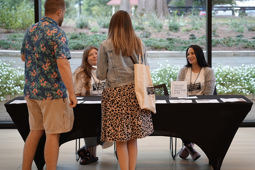 Photo of a man and a woman approaching two people seated behind a table.