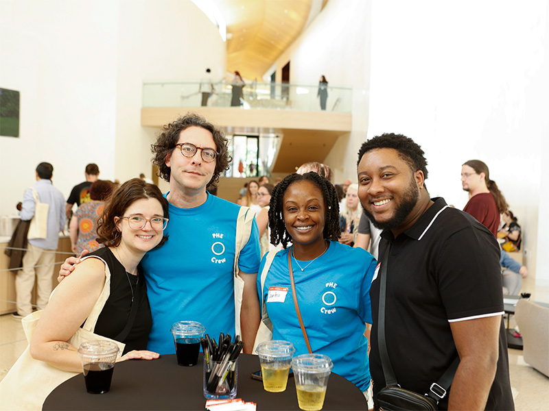 Photo of two women and two men posed and smiling together next to wine glasses on a black table.