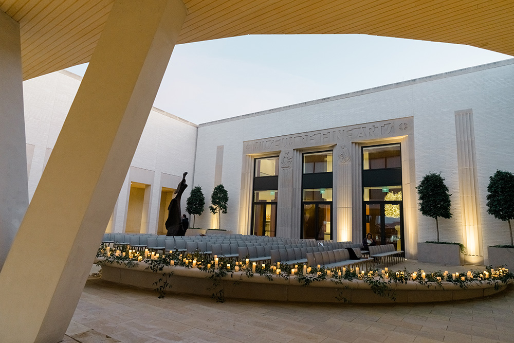 Photo of the AMFA Courtyard at sunset decorated with candles and rows of gray chairs for a wedding ceremony.