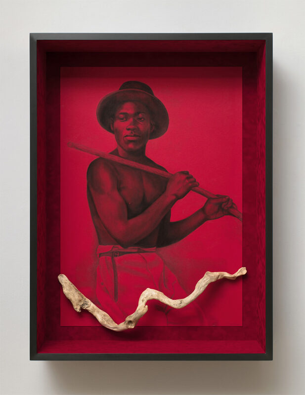 Photo of a drawing of a man on red paper in a red frame with a curved, light wooden stick attached to the bottom.