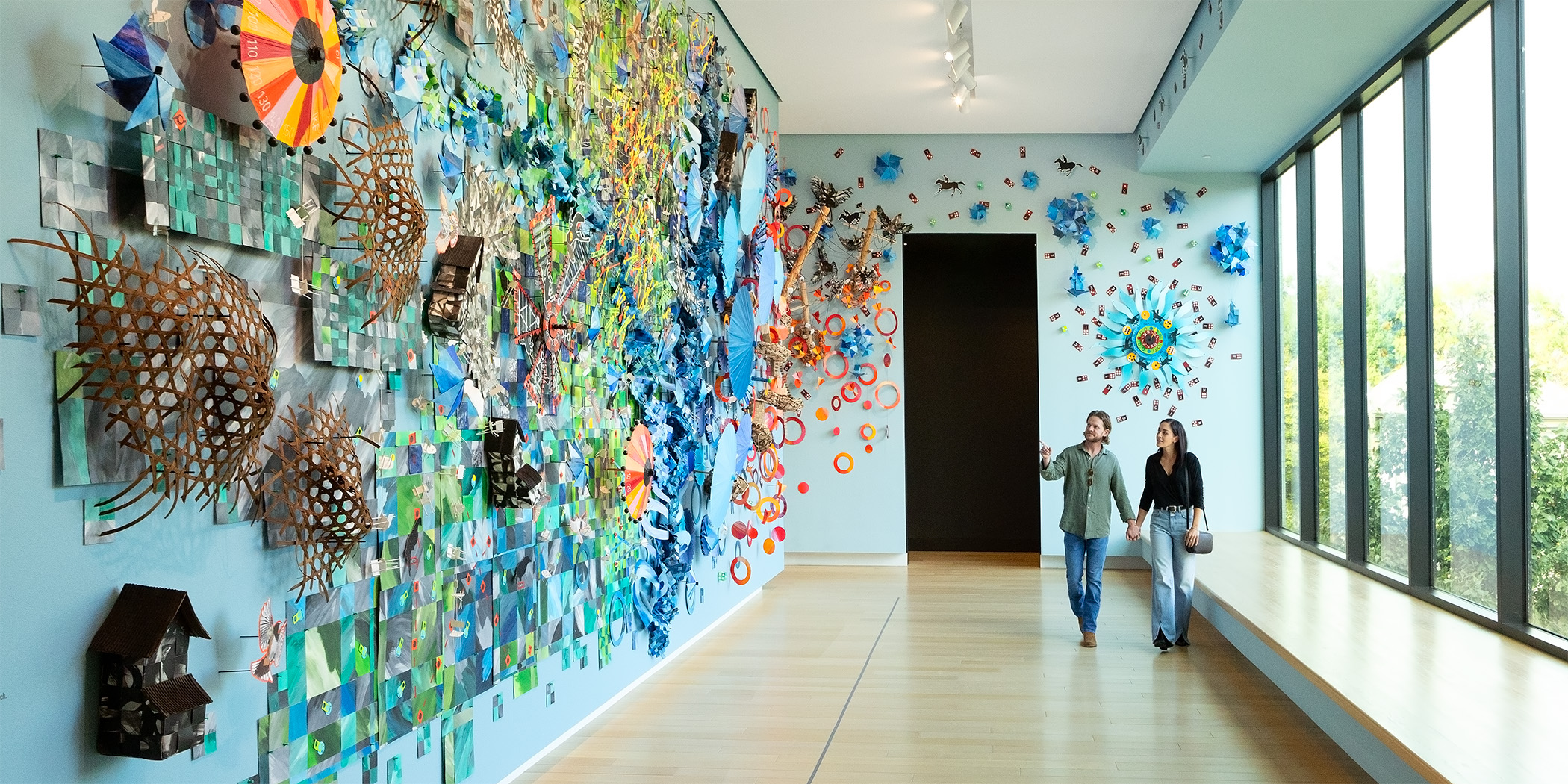 Photo of a man and a woman holding hands and walking in front of a large art installation in an art gallery at AMFA.