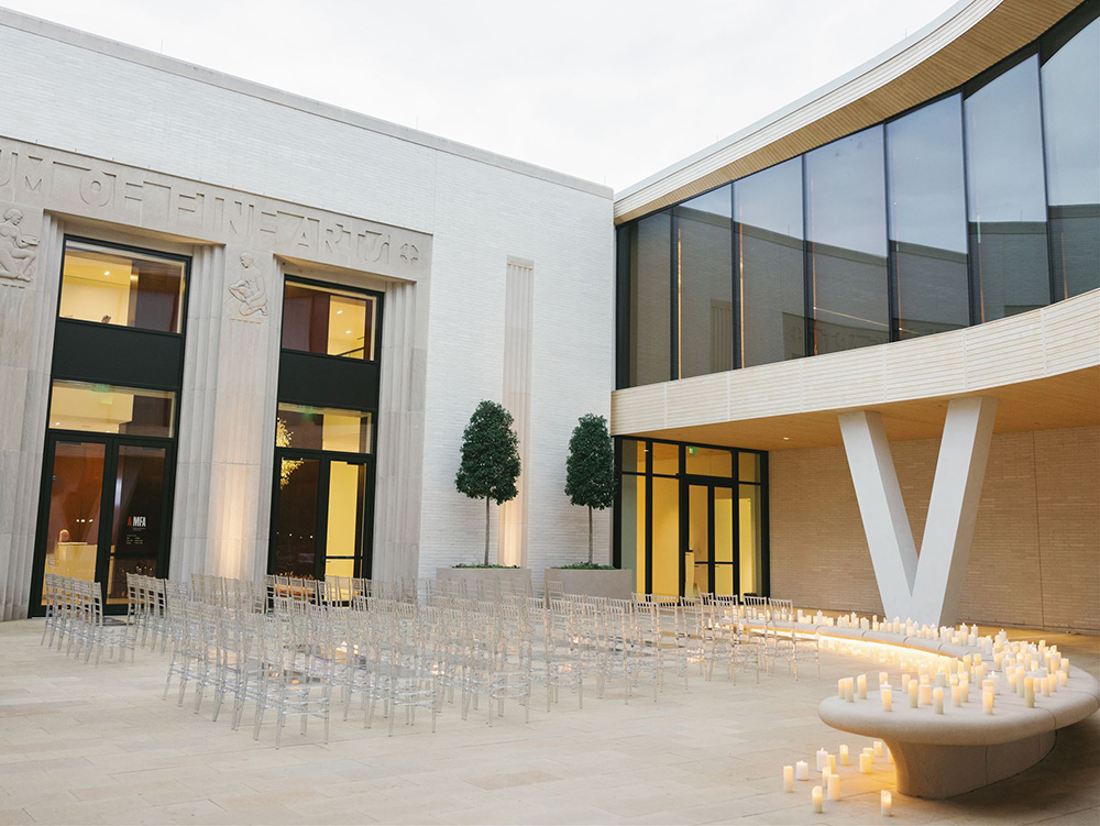 Photo of the Courtyard Entrance to the Arkansas Museum of Fine Arts decorated with rows of clear chairs and candles for a wedding ceremony.