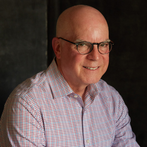 Photo of a smiling bald man wearing glasses and a button-down shirt.