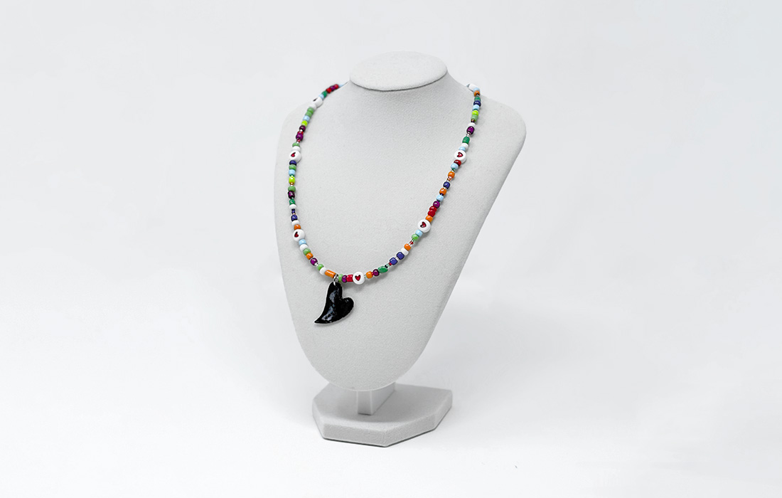 Photo of a beaded necklace with a large charm on a necklace stand.