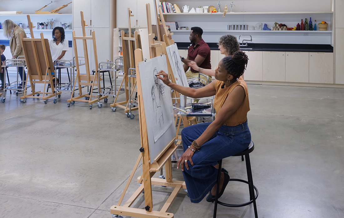 Photo of a group of adults sitting and drawing on easels in an art studio.