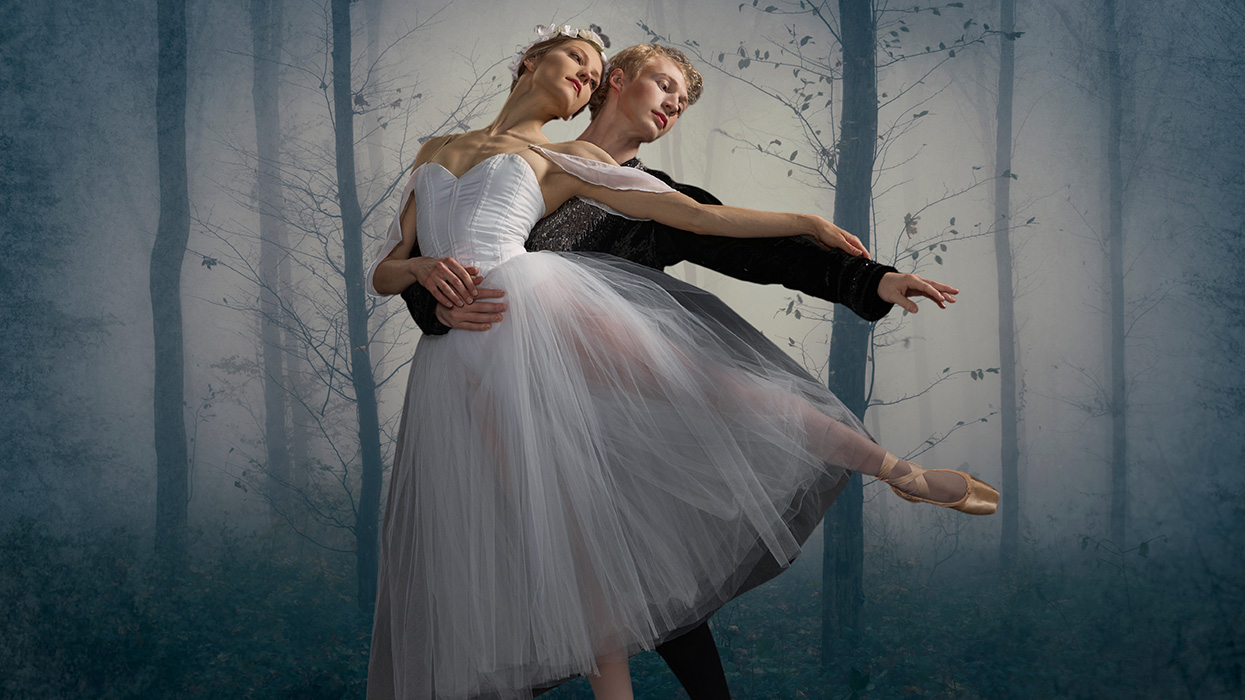 Photo of a male and female ballet dancer posed together dancing in front of a wintery forest background.