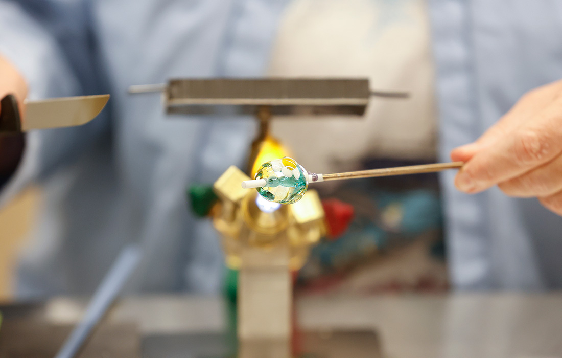 Close-up photo of a person making a glass bead on a rod over a flame.