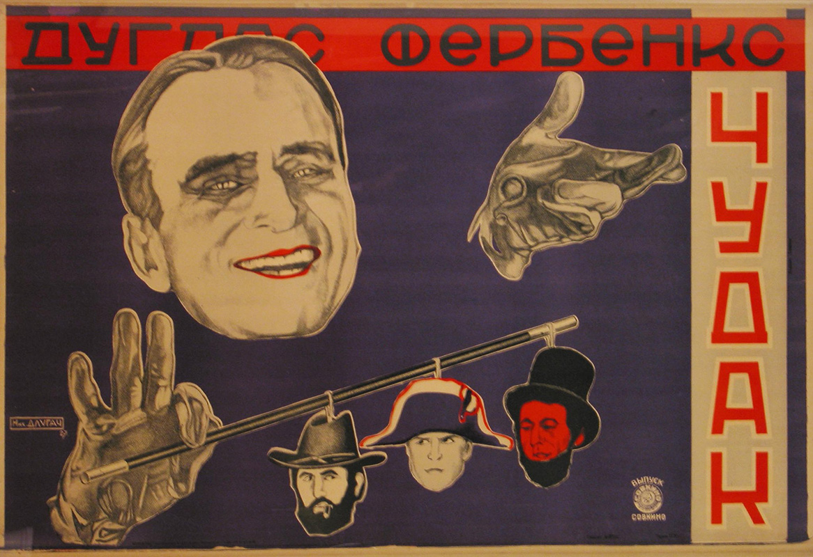 Photo of a 1920s Soviet poster depicting a simling man and a red banner with black lettering behind him.