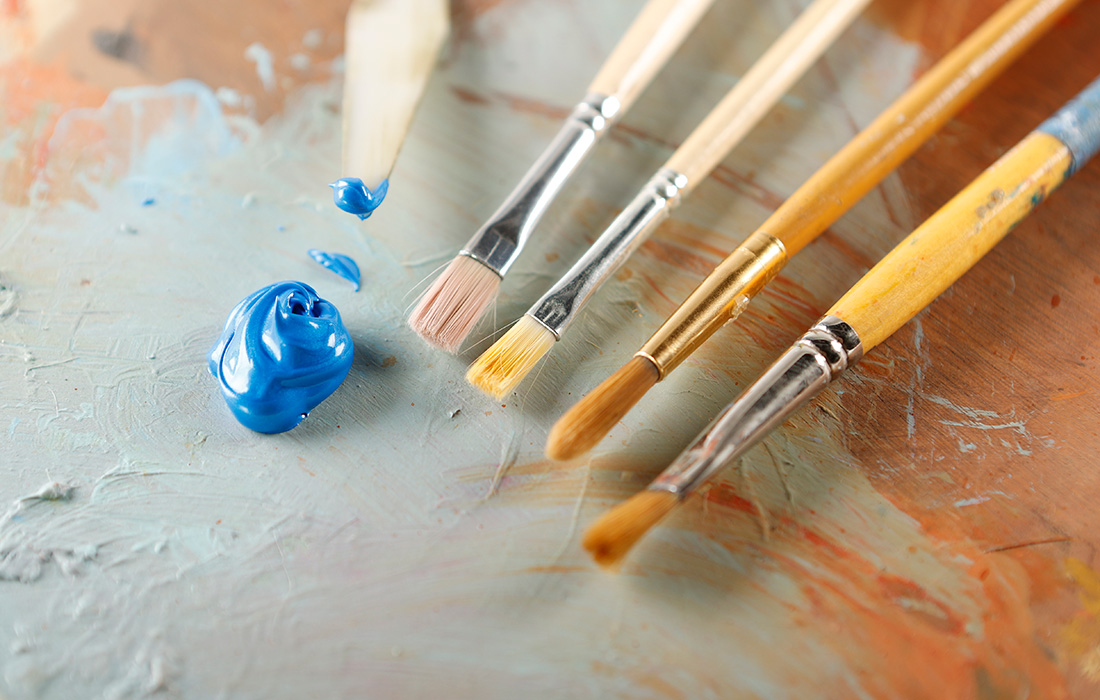 Photo of a dollop of blue paint on a palette next to several paint brushes.