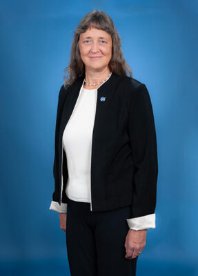 Photo of a woman with long gray hair and bangs wearing a black suit with a white blouse.