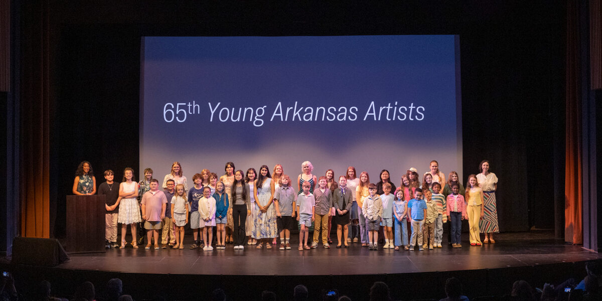 Photo of a group of young people posed together and smiling on a stage in front of a screen that says 65th Young Arkansas Artists.