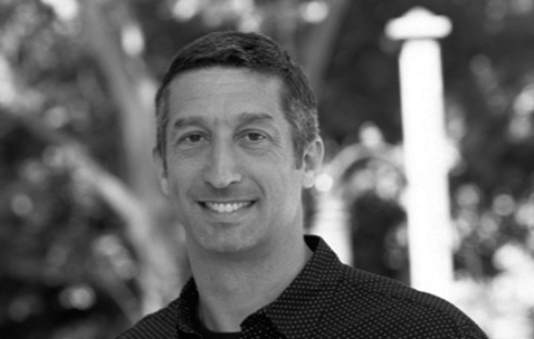 Black and white photo of a smiling man standing outdoors.