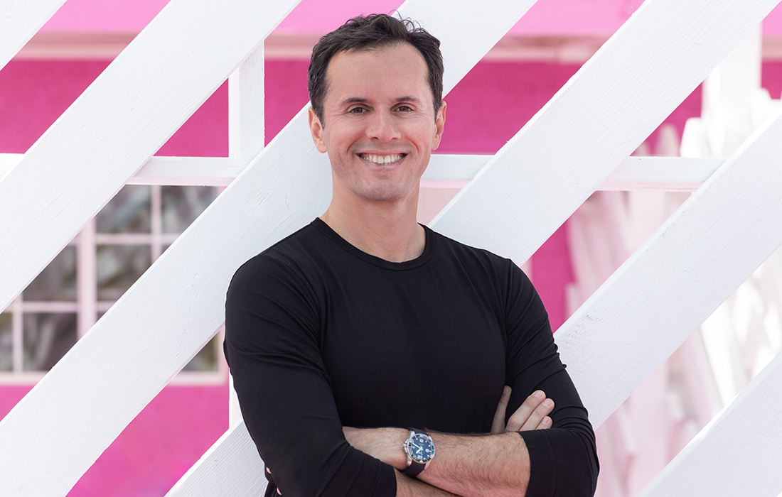Photo of a smiling man with short brown hair wearing a watch and a black long-sleeved shirt and posing with his arms crossed.