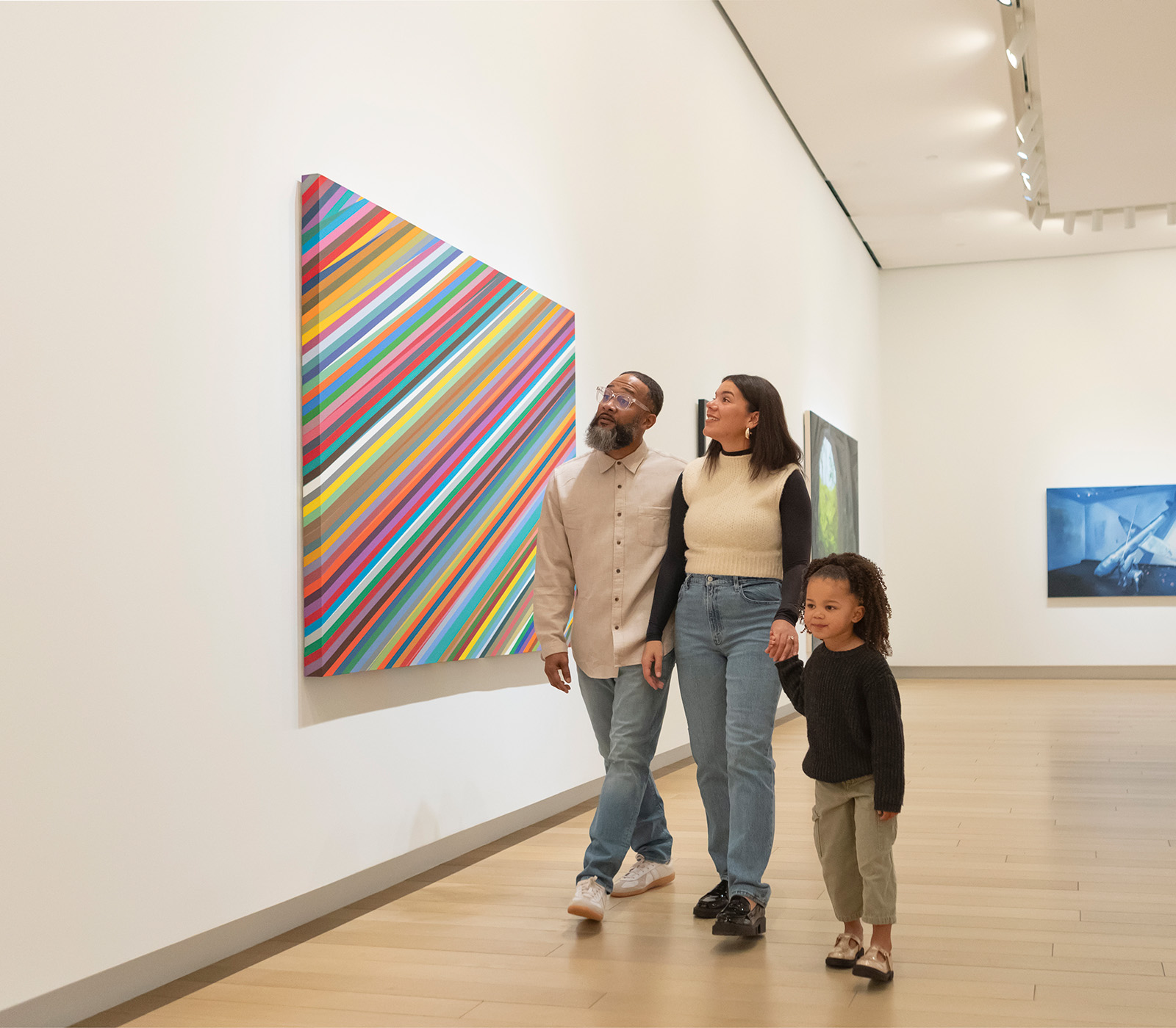 Photo of a man, woman, and child holding hands and walking through an art gallery.