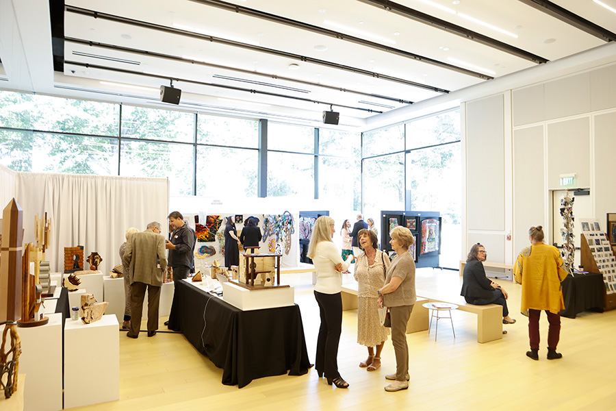 Photo of several booths set up at the AMFA Art Market in a large room with floor-to-ceiling glass windows.