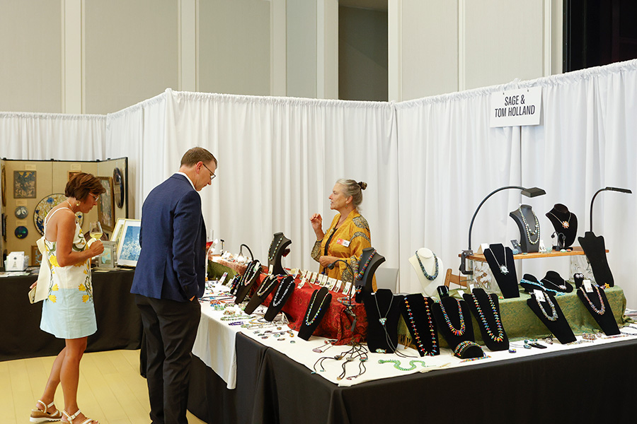 Photo of a man and a woman looking at necklaces on a table in a booth at the AMFA Art Market.