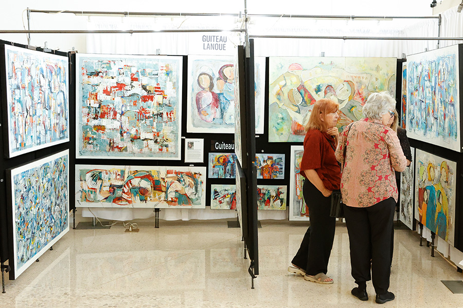 Photo of two women looking at large abstract painting set hanging in a booth at the AMFA Art Market.