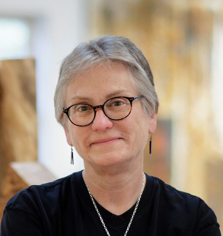 Photo of a woman with short gray hair wearing a black shirt and black rimmed glasses.