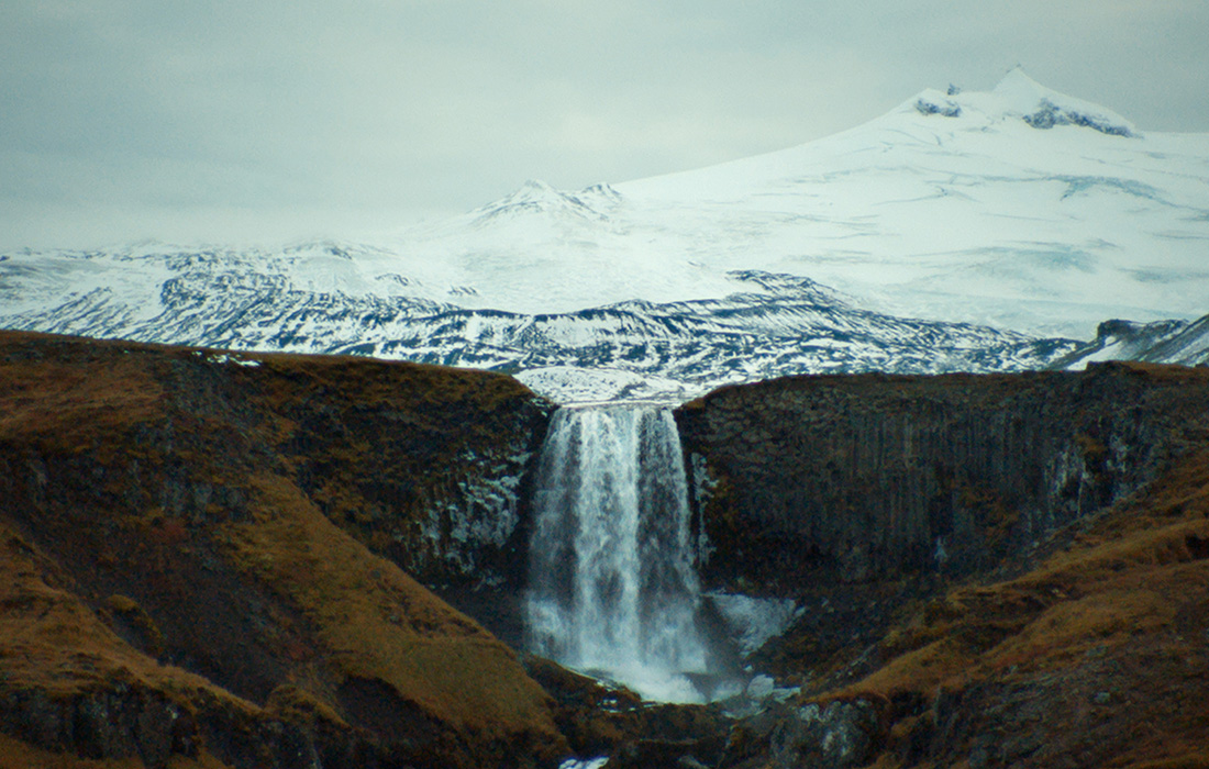 Film still of a glacial tongue behind a waterfall in a valley.