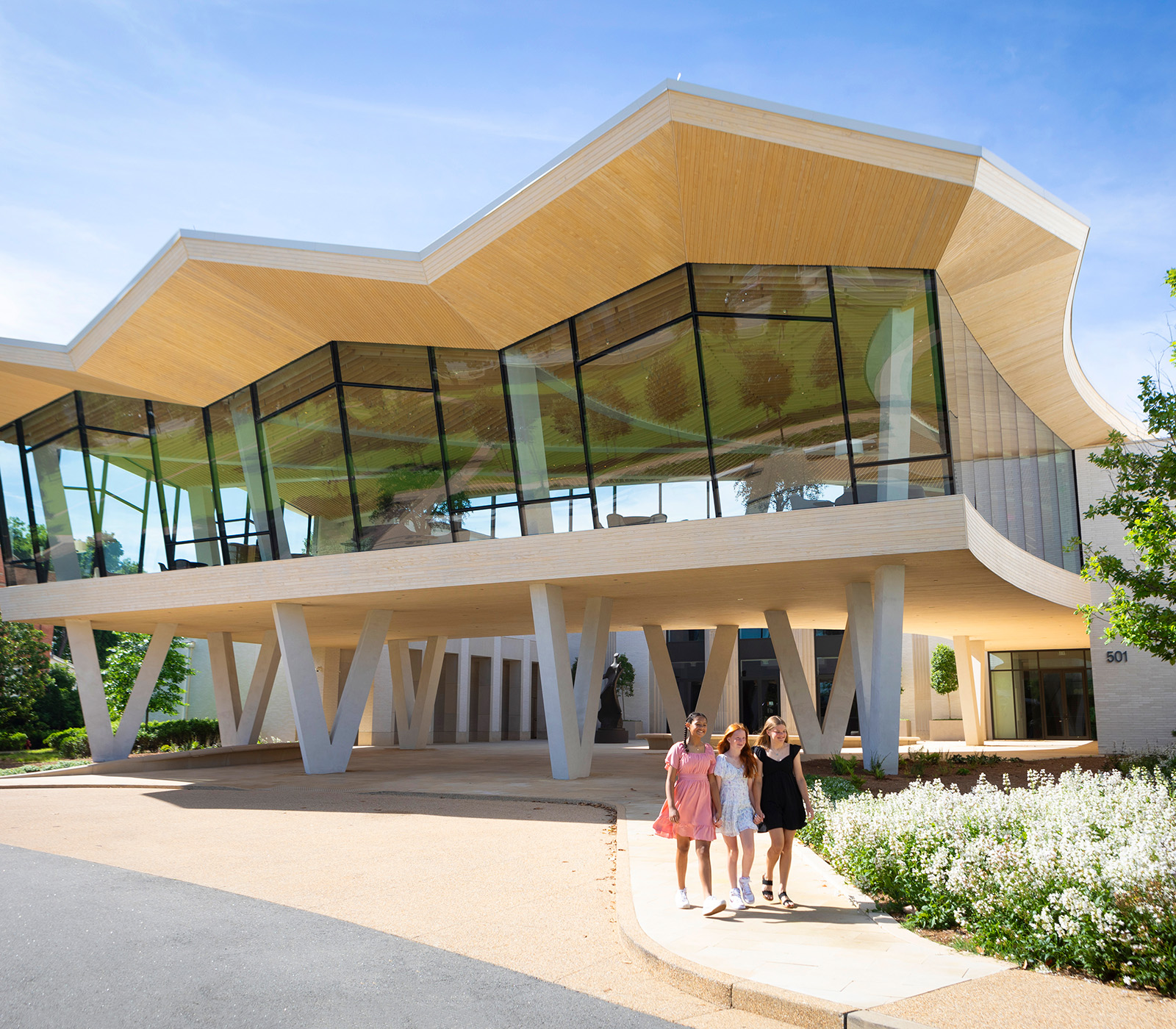 Photo of the Courtyard Entrance to AMFA. Three young girls are the in the foreground walking along a sidewalk lined with white flowers.