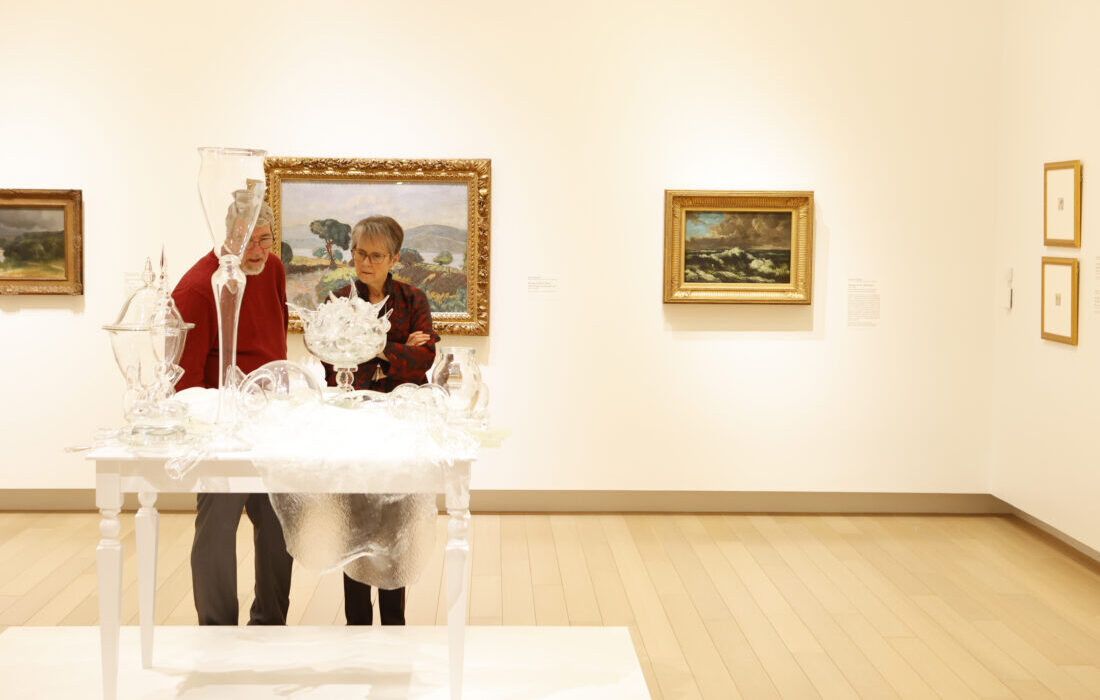 Photo of a man and a woman looking at a glass sculpture on a table in an art gallery.