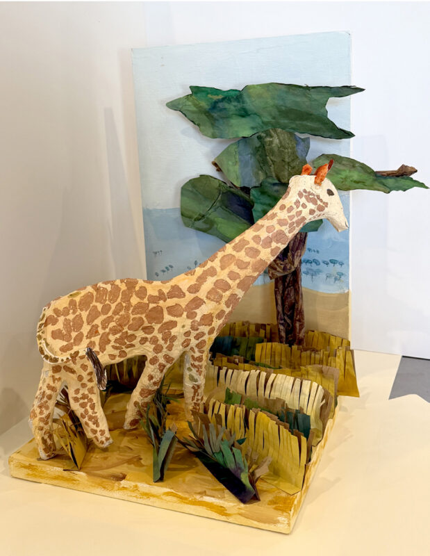 Paper mache sculpture of a giraffe on a savanna.