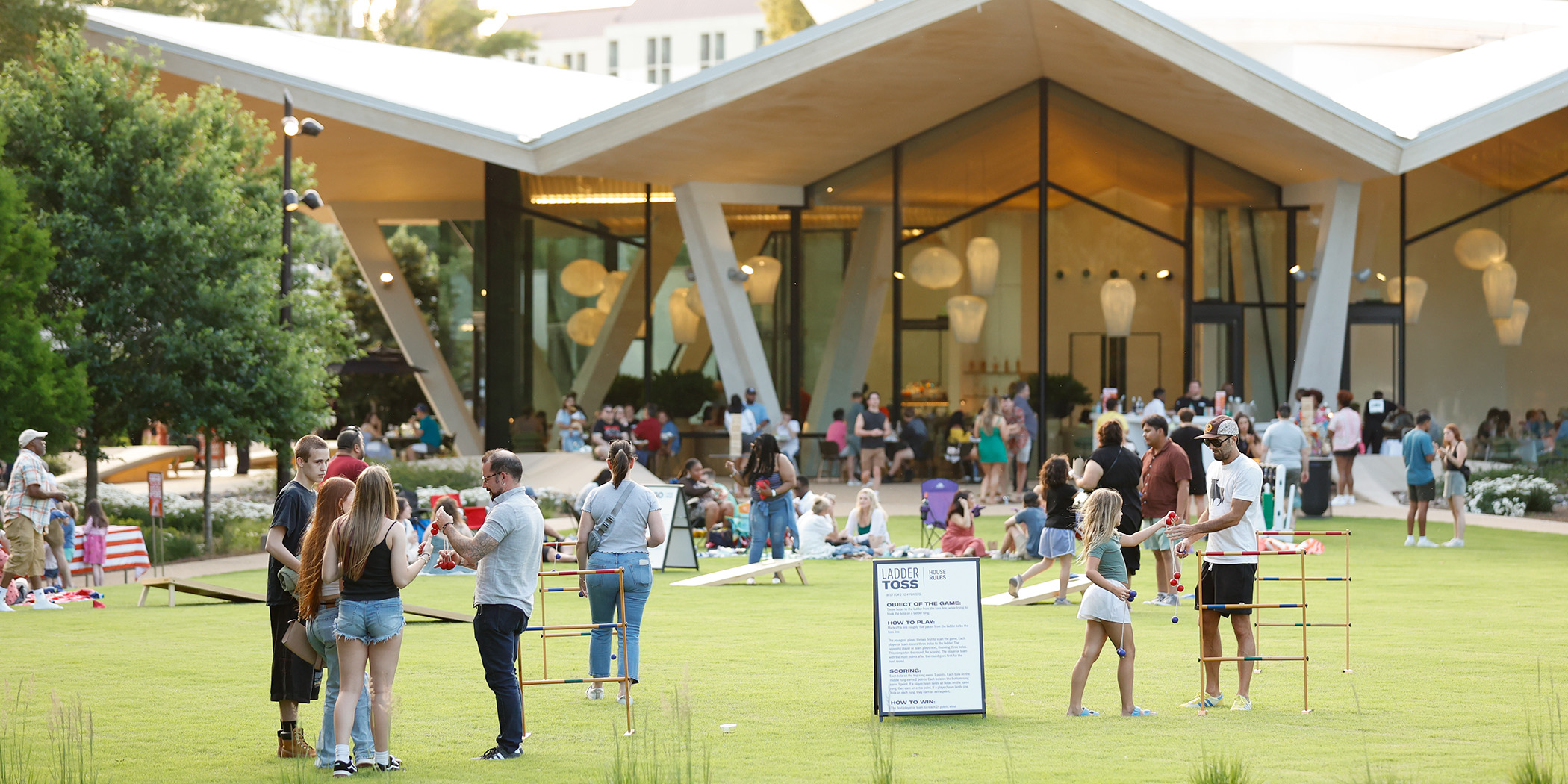 Photo of people playing lawn games, sitting on blankets, and standing in groups talking outside of the Arkansas Museum of Fine Arts on the Event Lawn.