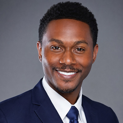 Headshot of a man in a dark suit and blue tie smiling in front of a gray background.
