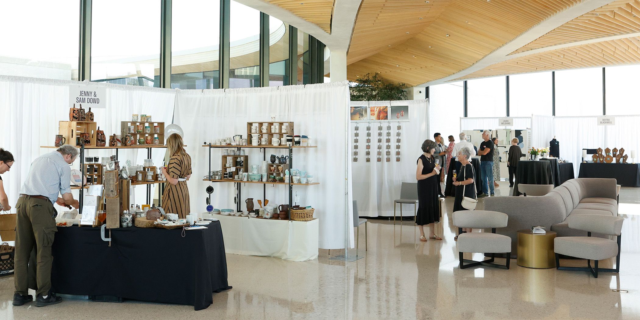 Photo of art booths divided by white curtains set up in an open airy room with tall ceilings and windows.