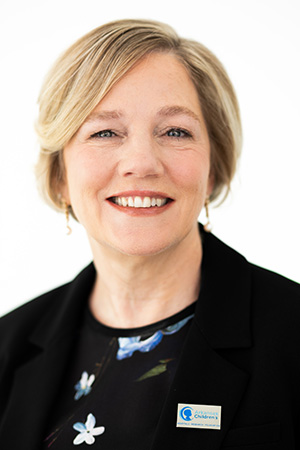 Headshot of a smiling woman with short blonde hair wearing a black floral blouse and a black jacket with an Arkansas Children's lapel pin.