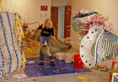 Photo of a woman with short blond hair handling large mixed media sculptures in an art studio.