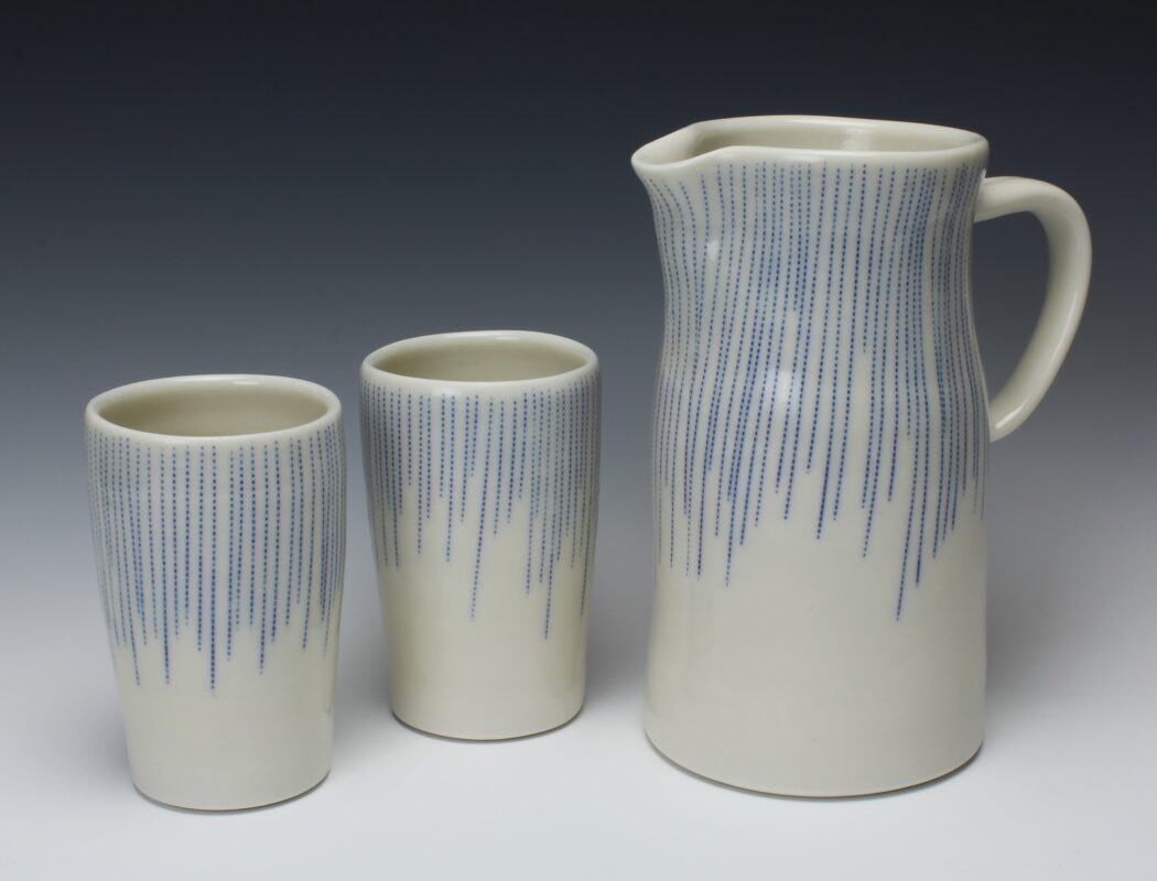 Photo of a two ceramics cups and a ceramic pitcher decorated with a white glaze and blue dotted lines.