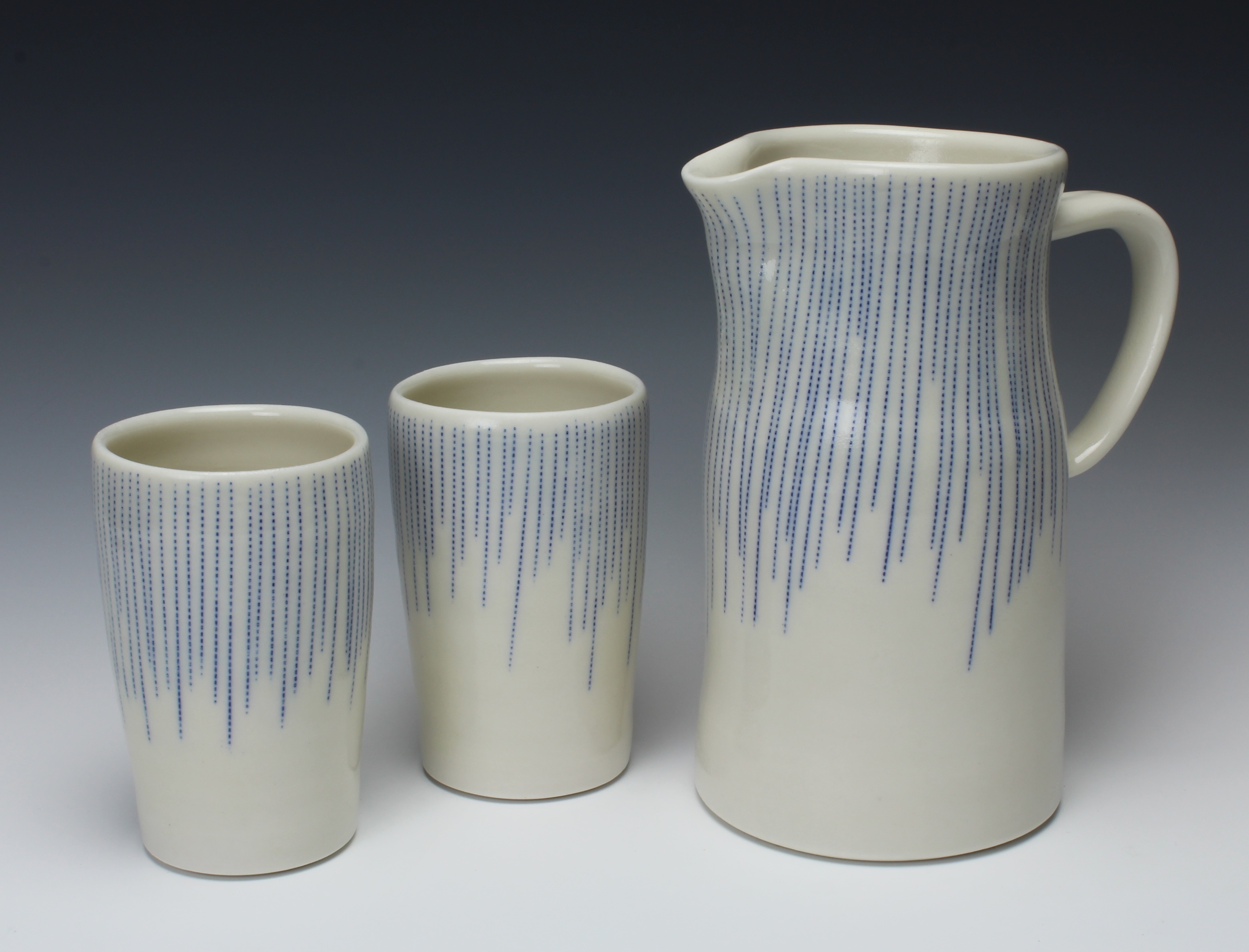 Photo of a two ceramics cups and a ceramic pitcher decorated with a white glaze and blue dotted lines.