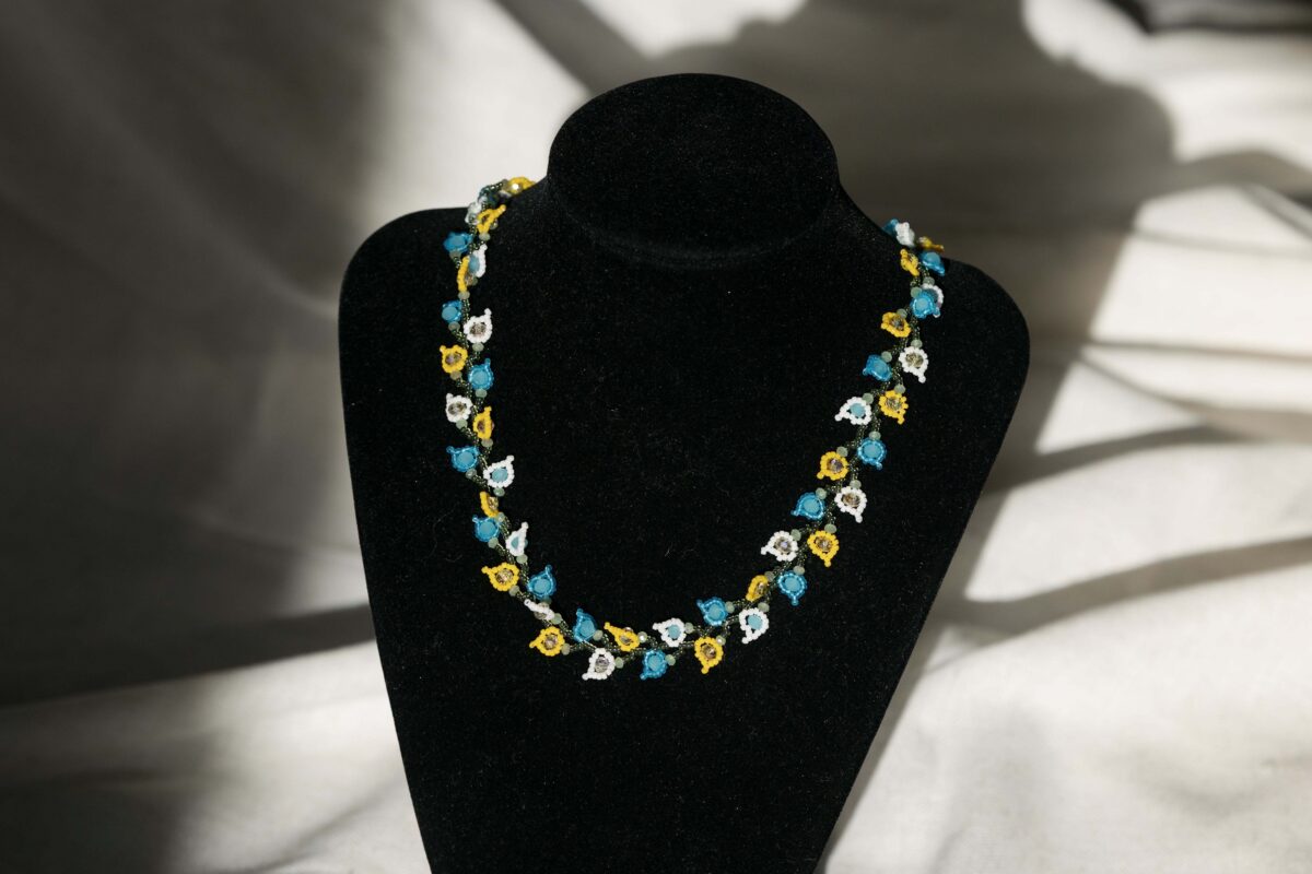 Photo of a necklace comprised of small glass beads in the shape of flower petals sitting on a black pedestal.