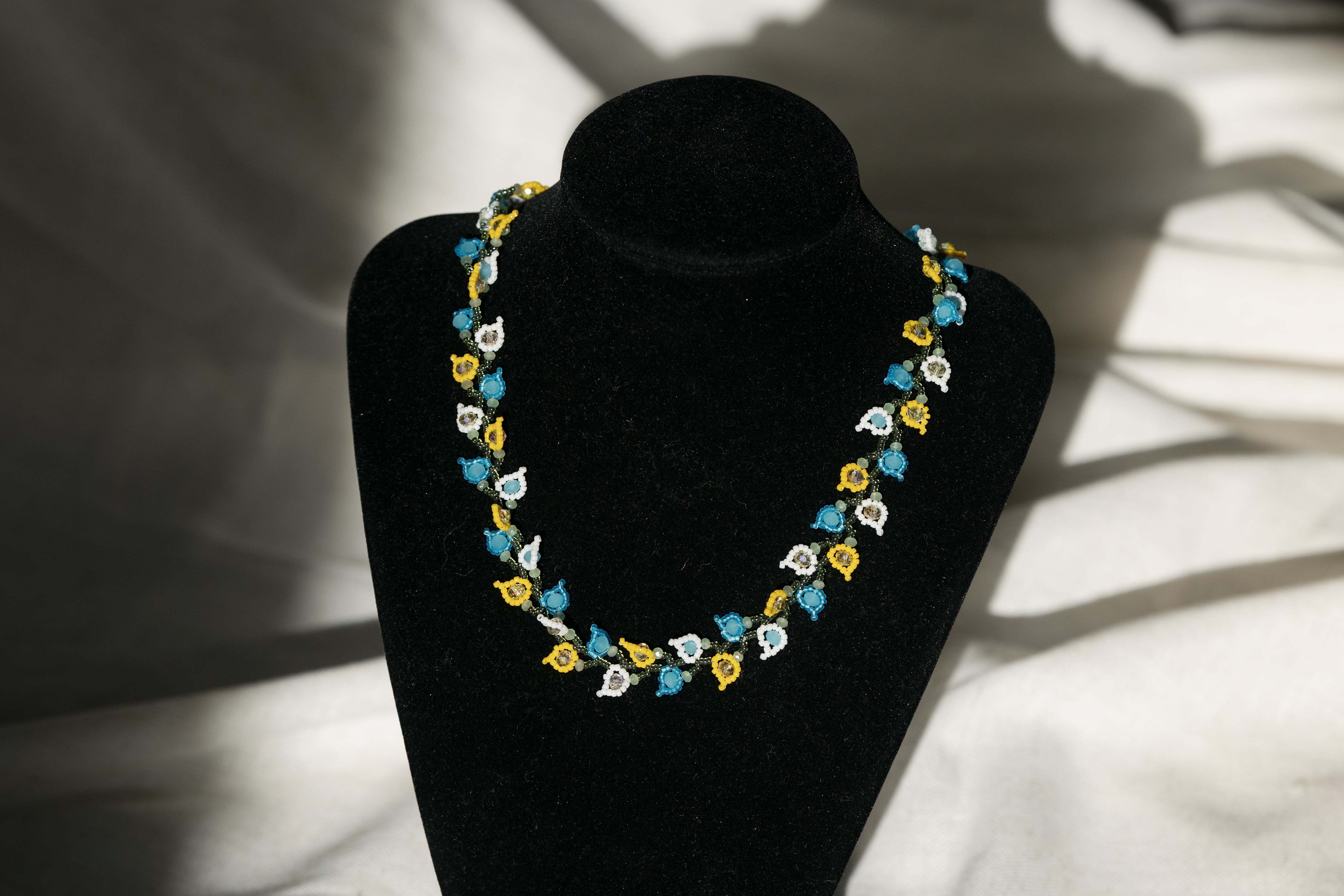 Photo of a necklace comprised of small glass beads in the shape of flower petals sitting on a black pedestal.