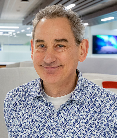 Headshot of a smiling man with short gray hair wearing a blue and white patterned button-down shirt.