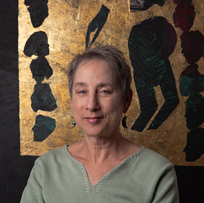 Headshot of a woman with short hair wearing a light green shirt and posing in front of an abstract gold and black painting.