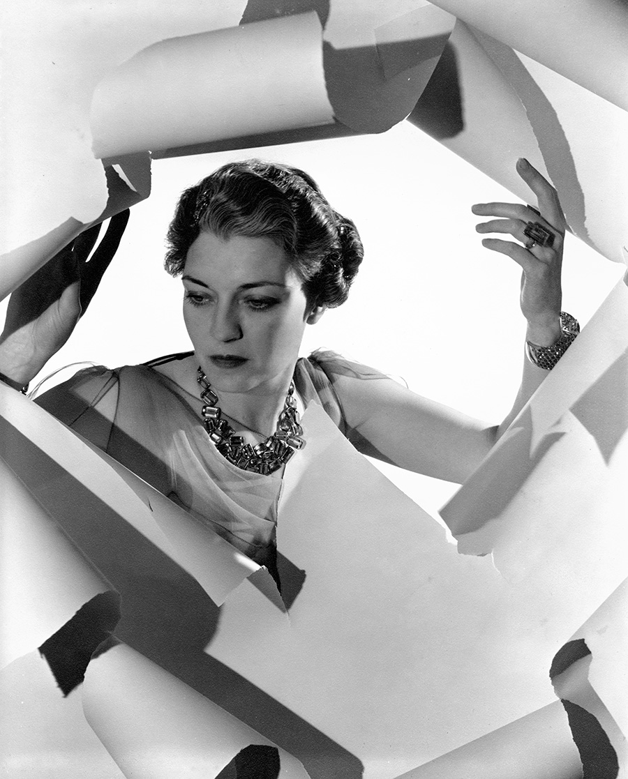 Black and white photo of a woman posing behind a sculpted frame of torn paper.