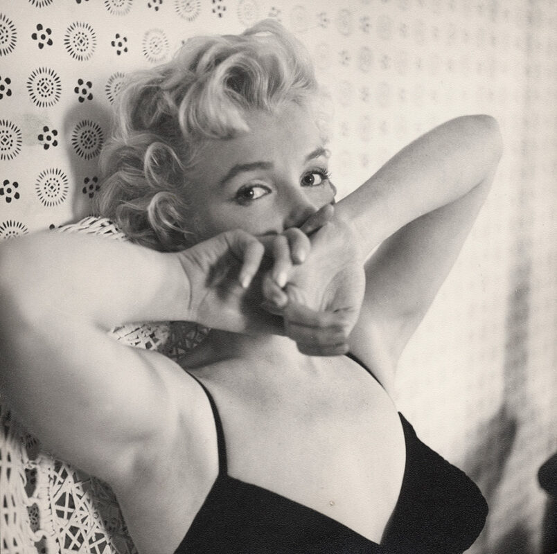 Black and white photo of Marilyn Monroe wearing a black tank top and holding her hands over her mouth.