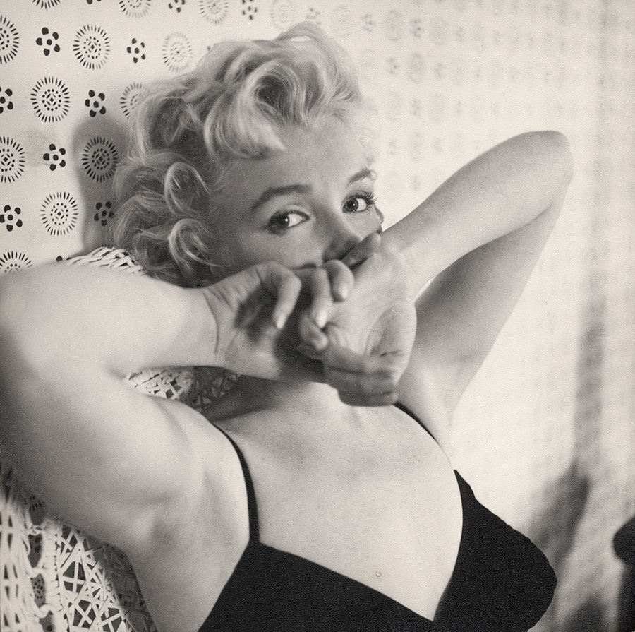 Black and white photo of Marilyn Monroe wearing a black tank top and holding her hands over her mouth.